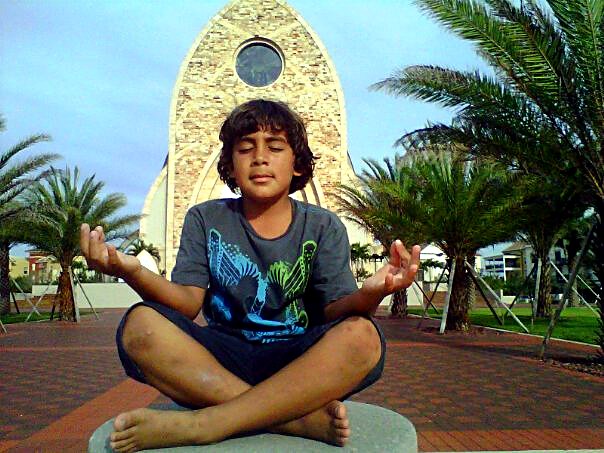 A young meditator in lotus pose in front of a stone chapel, a family photo shared by Christine