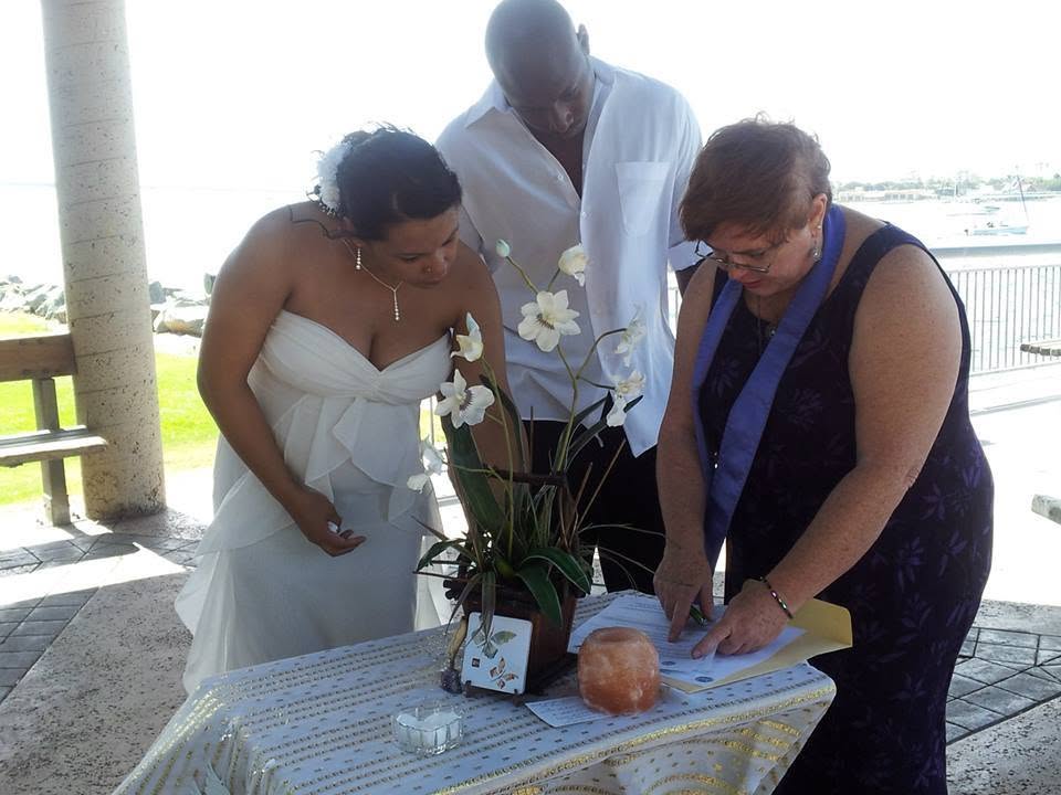 Rev. Christine signing the marriage license with a bride and groom by the water