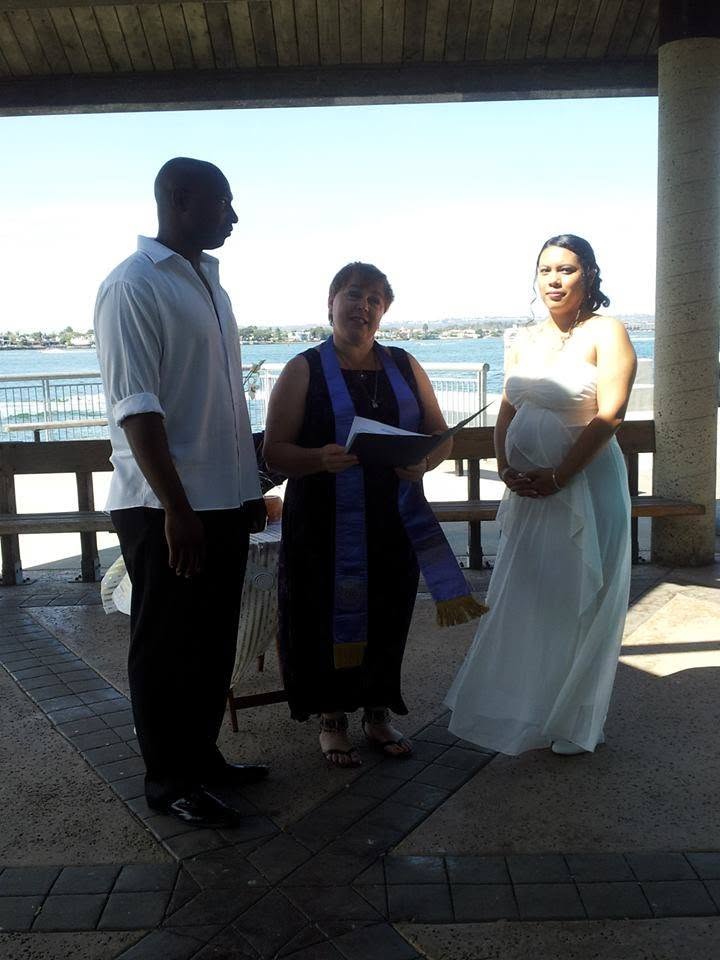 Rev. Christine reading the ceremony between a bride and groom by the water